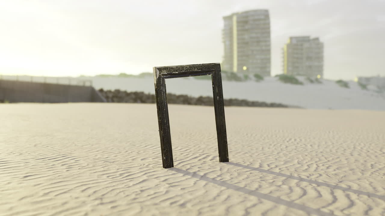 Unique black frame standing alone on sandy beach at sunset near buildings