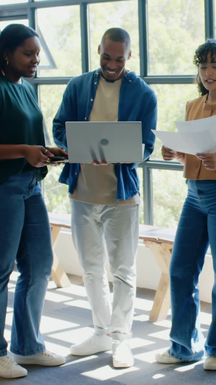 Vertical video: Shifting man showing laptop while casual team comparing tablet and papers in office