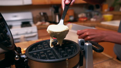 young man making waffles for the family - spoons batter on the waffle iron in slow motion