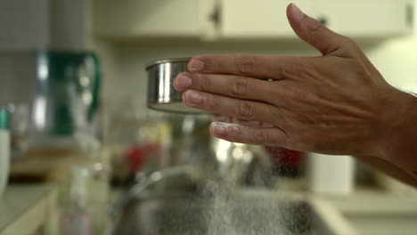 slow motion shot of a man using a flour sifter where flour particles are released and fall on the kitchen table