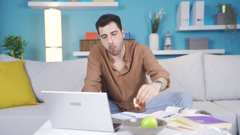 Happy-young-man-working-at-home-and-eating-fruit.