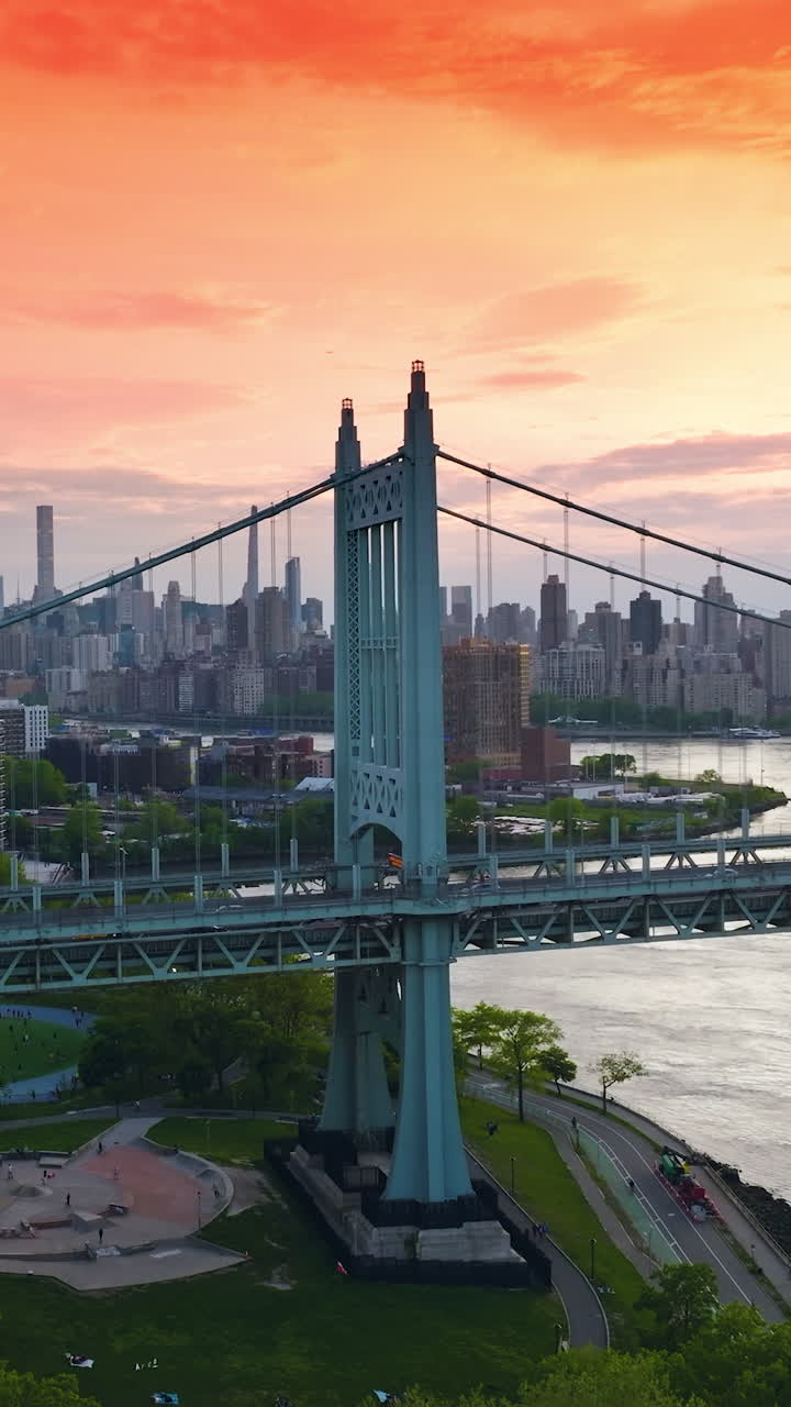 Magnificent light blue bridge with moving transport. New York skyline of skyscrapers under the pink orange sky. Vertical video