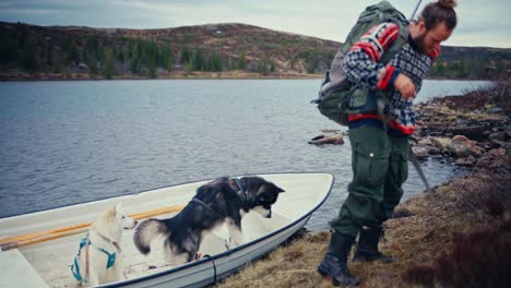 a person with his dogs going down the rowing boat from a lake. static shot