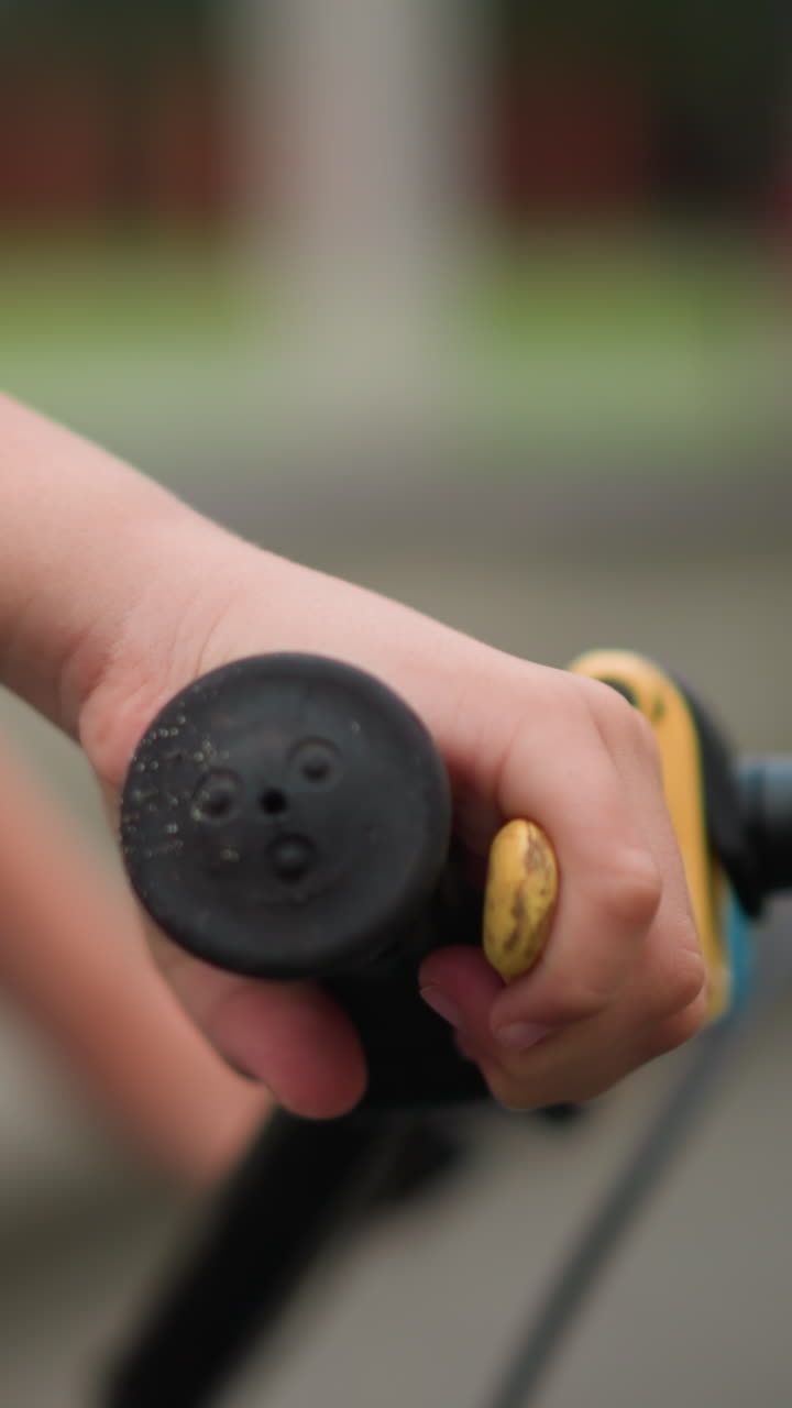 un primer plano de la mano de un niño agarrando y soltando el mango del freno de una bicicleta, con un fondo borroso