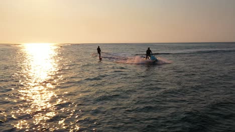 water sports aerial, silhouette of jet ski pulling man hydro foiling on calm ocean during sunrise