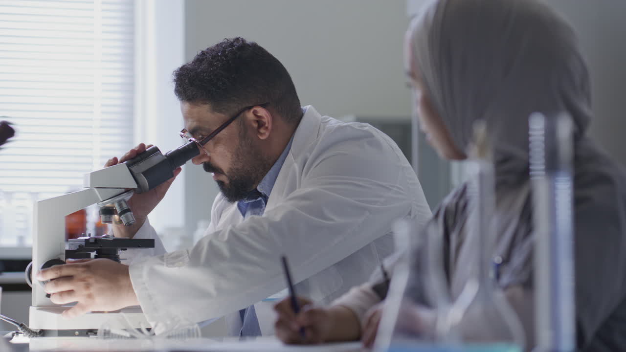 Scientist Working with Microscope and Talking to Colleague in Laboratory