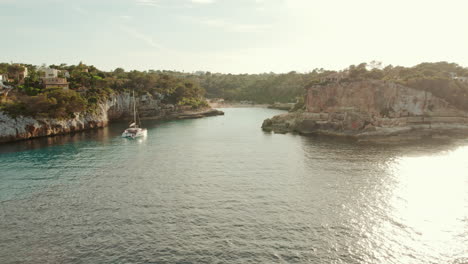 catamaran boat floating in the calm and glistening waters of sea in cala llombards, mallorca, spain