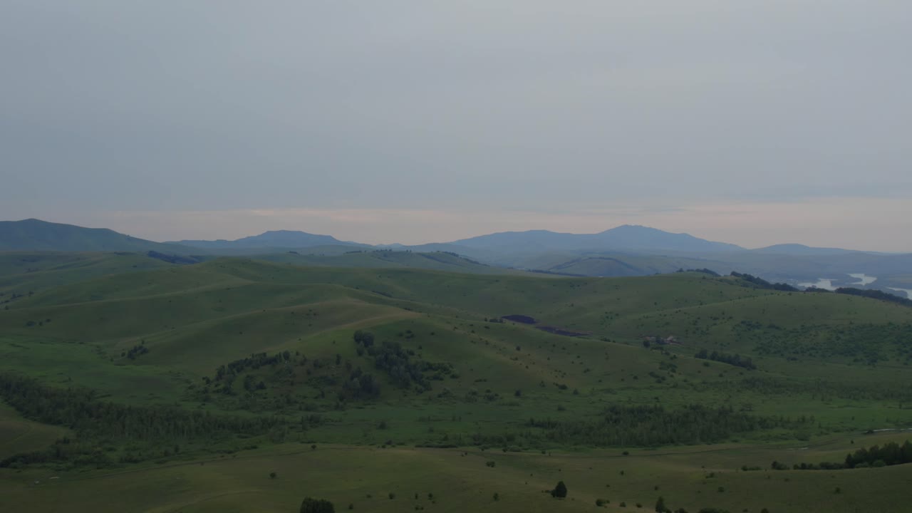 Wide landscape footage of rolling green hills, valleys and distant mountains under cloudy sky in Altai, Russia, natural countryside scenery with calm atmosphere