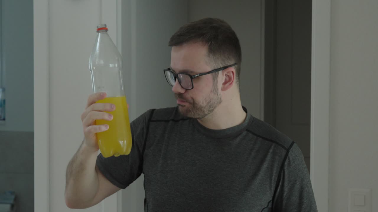 Hombre adulto bebiendo directamente de una botella grande de refresco amarillo, destacando el consumo excesivo de azúcar, hábitos poco saludables y el riesgo potencial de obesidad y diabetes