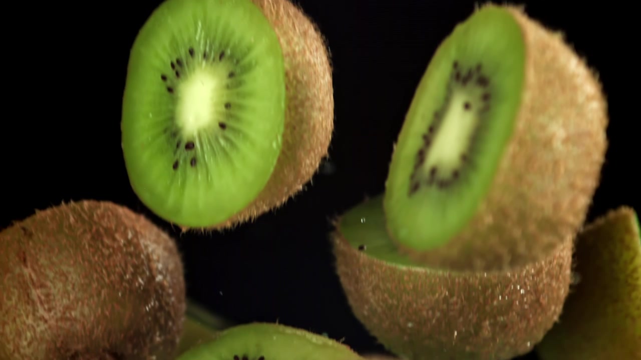 Kiwis frescos cortados cayendo con gotas de agua a cámara lenta