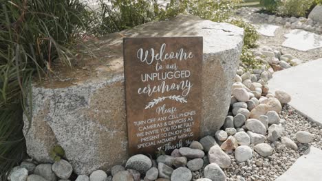 „Willkommen-Bei-Einer-Unplugged-Zeremonie“-Holzschild,-Das-An-Einem-Großen-Felsen-Inmitten-Eines-Gartenzeremoniellortes-Im-Freien-Im-Le-Belvédère-In-Wakefield,-Quebec,-Kanada,-Ruht