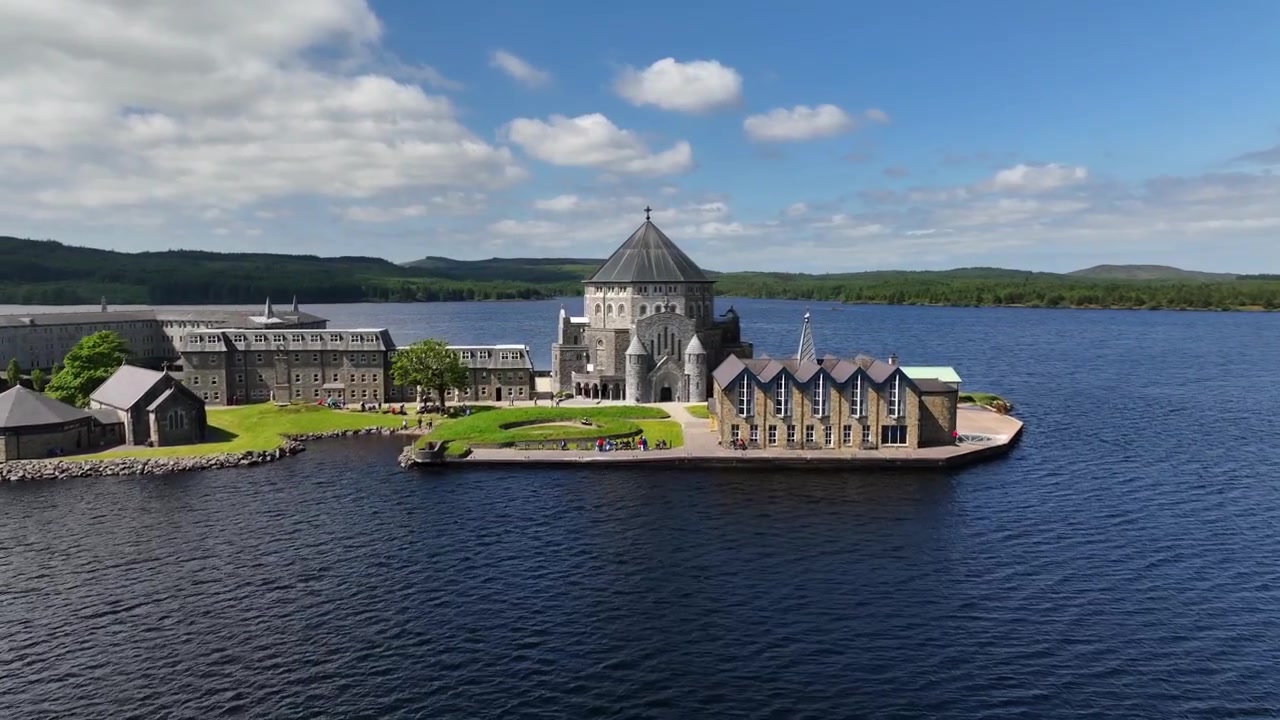 Lough Derg, Donegalin kreivikunta, Irlanti, kesäkuu 2023. Drone etenee lehtevän rantaviivan yläpuolella, ja St. Patrick's Purgatory Station Islandilla on keskellä järveä.