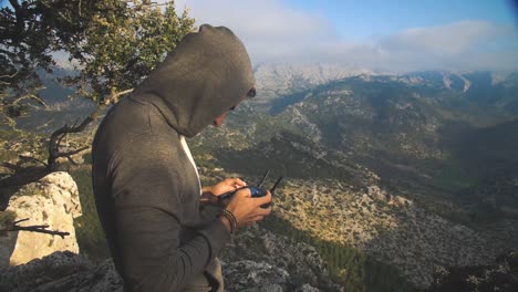 slow motion shot of a mysterious man standing in wilderness and flying his drone with drone remote controller in his hands with a breathtaking background