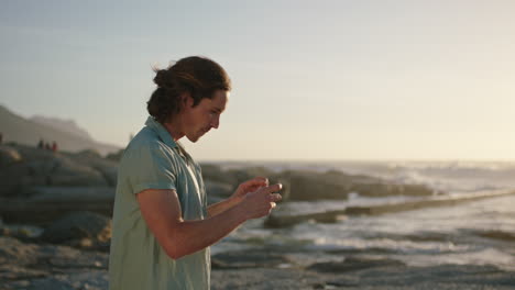 attractive man taking photo using phone photographing beach at sunset