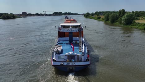 Drone-aerial-shot-following-large-container-ship-from-the-back-trees-and-landscape-in-the-distance