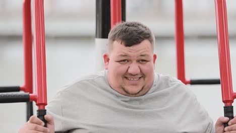 a young overweight man is working out doing exercises on outdoor exercise machine in a green area a young overweight man is working out doing exercises on an outdoor exercise machine in a green area a fat man struggles with excess weight exercises for hands