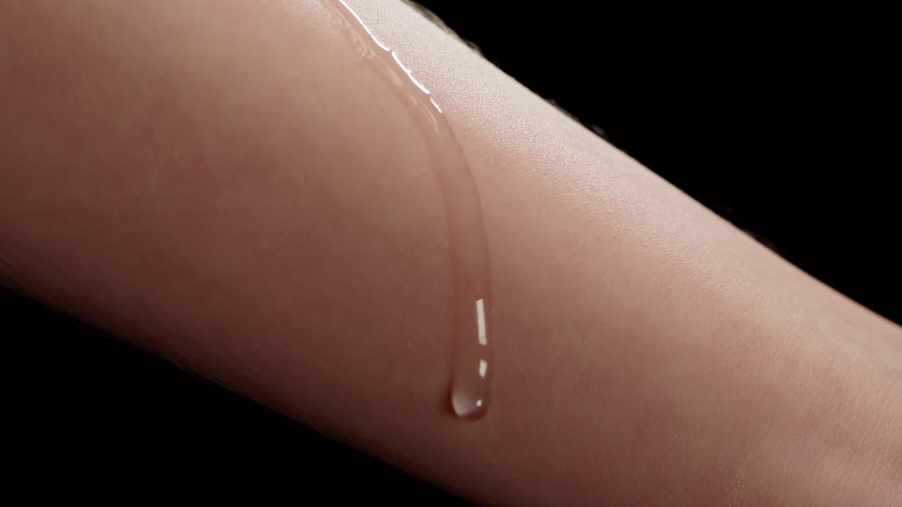 Gel cosmetico trasparente che cola lentamente lungo un braccio umano