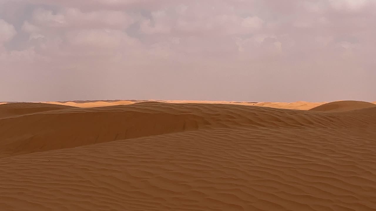 Contrasto di colori del deserto del Sahara con il sole che splende e nuvole che si muovono su una superficie sabbiosa ondulata