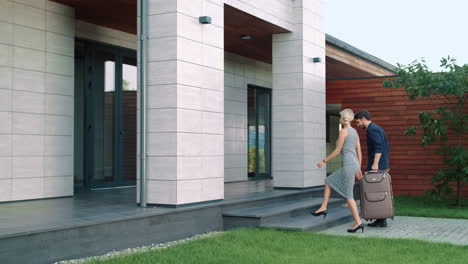 beautiful couple entering luxury house with suitcase. tourist couple coming home