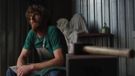 Tired-caucasian-male-blacksmith-taking-rest-in-workshop