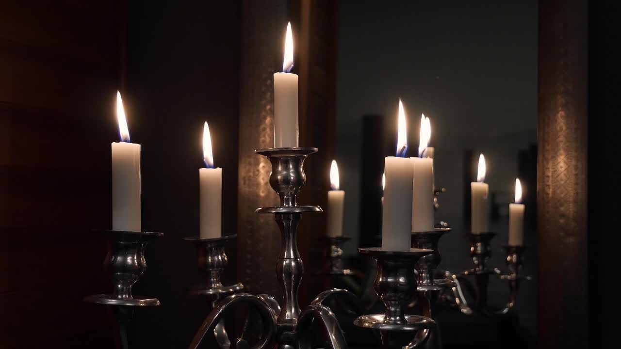 toma a mano media de algunas velas en un candelabro de plata con paredes de madera y un espejo en el fondo