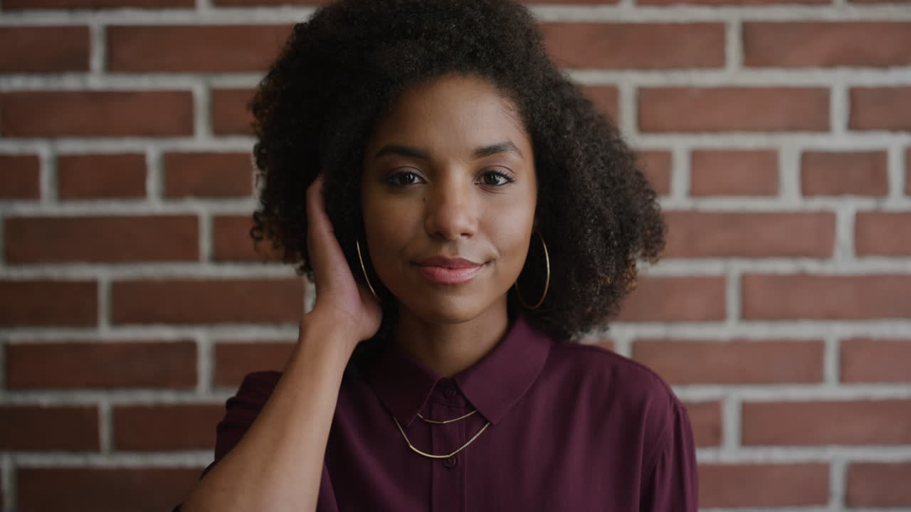 ritratto elegante giovane donna afroamericana sorridente che corre con la mano attraverso i capelli godendo di uno stile di vita indipendente felice trendy donna nera afro acconciatura muro di mattoni sfondo