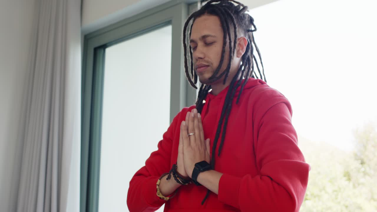 Man bringing hands together in prayer by sliding glass door in softly lit room wearing smartwatch
