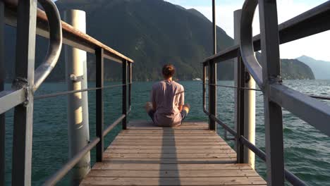 guy meditates on a deck near water