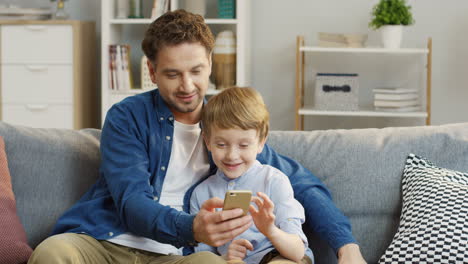 Handsome-Man-Teaching-His-Little-Son-To-Play-A-Game-On-The-Smartphone,-Father-And-Boy-Spending-Time-Together
