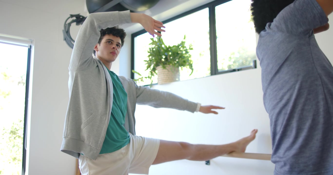 Diverse male duo stretching at bright studio, starting with left leg on barre, practicing balance