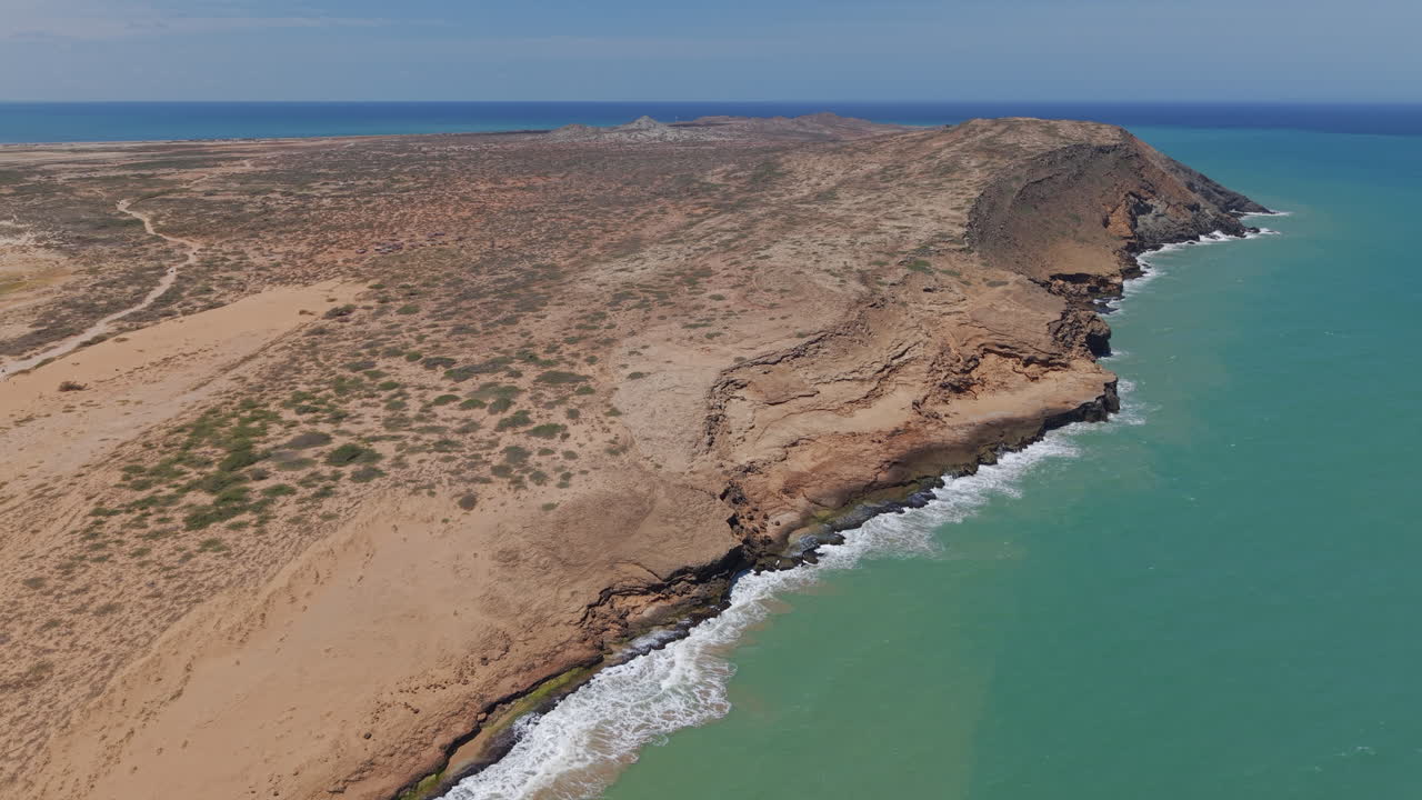 Spettacolari riprese aeree della costa frastagliata di Cabo de la Vela a La Guajira, Colombia, che mostrano drammatiche scogliere desertiche, acque caraibiche turchesi e cieli soleggiati e senza nuvole. Video nitido da drone