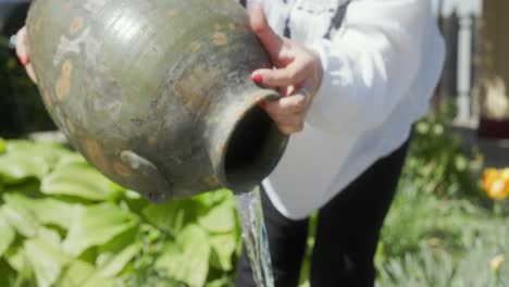 mujer regando plantas con jarro de barro nativo - de cerca