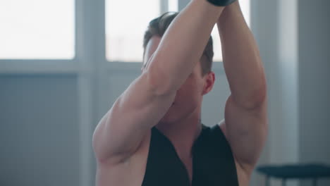 closeup of young man with belt tied around wrist dancing sensually in bright loft studio windows, casting soft light on bare arms and sculpted torso, showing confident movement