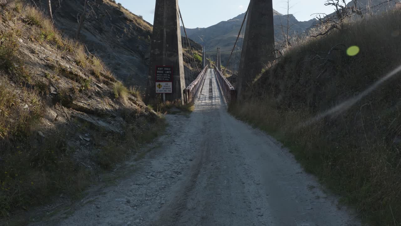 A dirt road leading to an old bridge above a valley on a sunny summer day at Skippers Canyon, Queenstown, New Zealand.