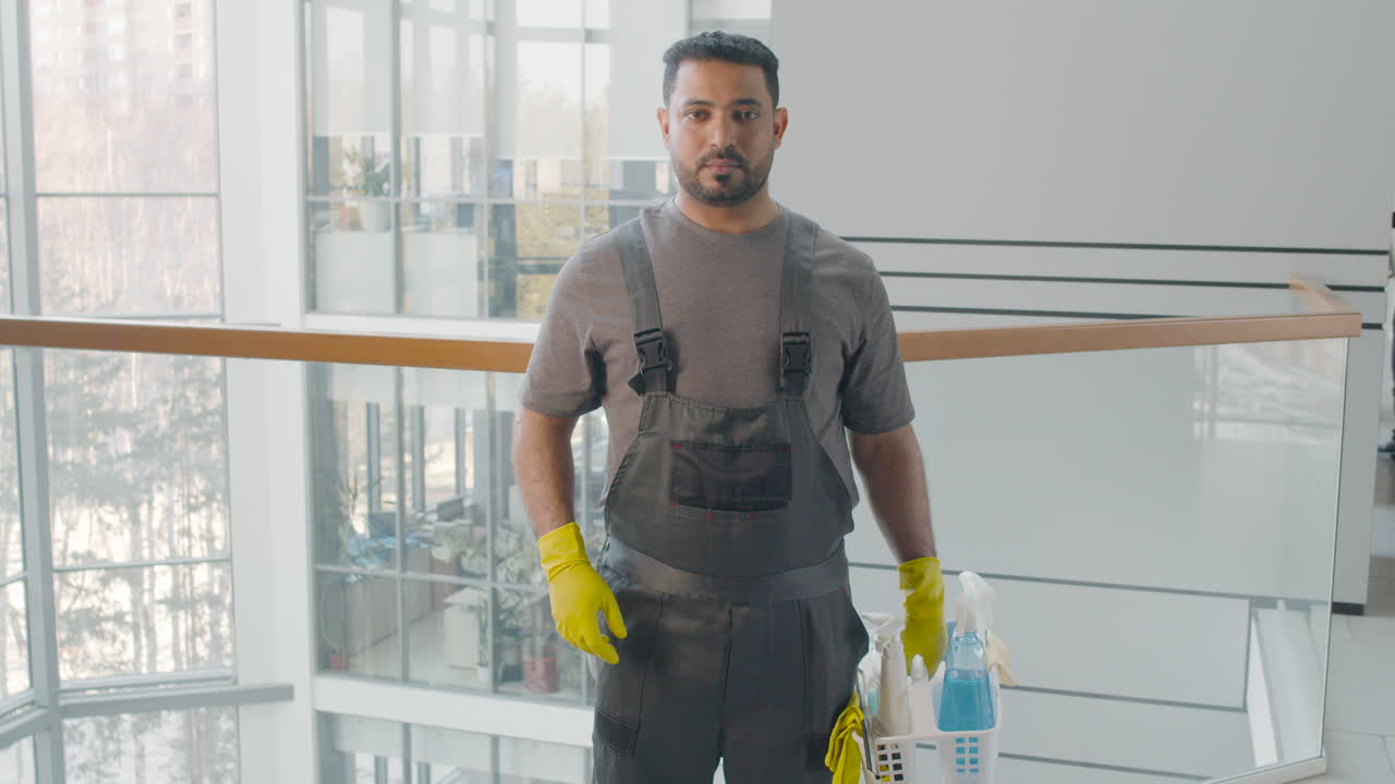 retrato de un limpiador árabe posando y mirando la cámara mientras sostiene productos de limpieza dentro de un edificio de oficinas