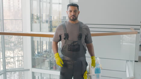 portrait of arabic cleaning man posing and looking at camera while holding cleaning products inside an office building