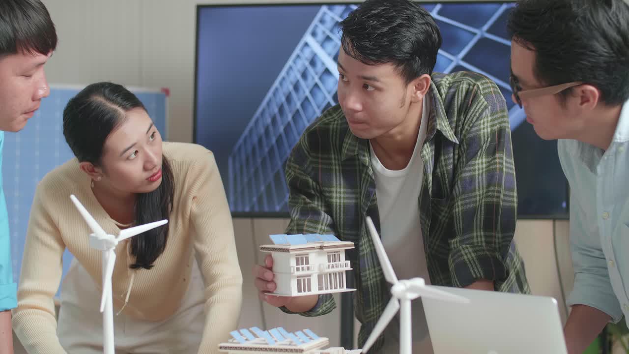 아시아 엔지니어 그룹이 사무실에서 태양 전지판을 가진 작은 집 모델에 대한 회의를 하고 있습니다.