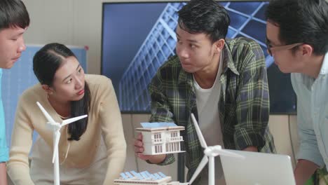 close up of asian engineers group having a meeting about the model of small house with solar panel at the office