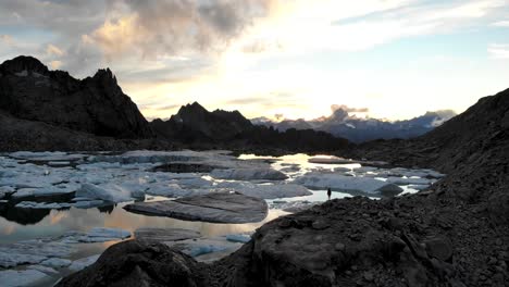 aerial flyover above a lake full icebergs from a melting glacier in remote parts of the swiss alps with a hiker enjoying the sunset glow and view
