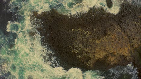 drone descends over the famous honeycomb rock formation at giants causeway, waves crashing as the shot moves from wide to close-up
