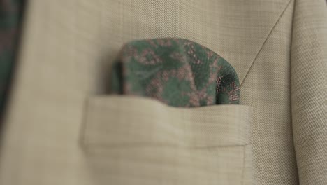 close up of a beige suit jacket with a green patterned tie and pocket square, highlighting sophisticated wedding attire