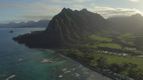 aerial view of the kualoa ranch and valley with the iconic mountain as seen above the turquoise pacific ocean during sunset