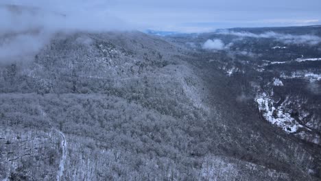 flying through clouds over snow-covered mountains and forests in a beautiful mountain valley during winter on a cloudy day