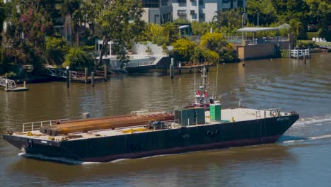 a tugboat manoeuvres a flat deck construction barge that transporting reinforced steel pylons up a river