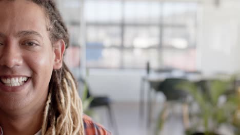 portrait of happy biracial casual businessman with dreadlocks in office with copy space, slow motion