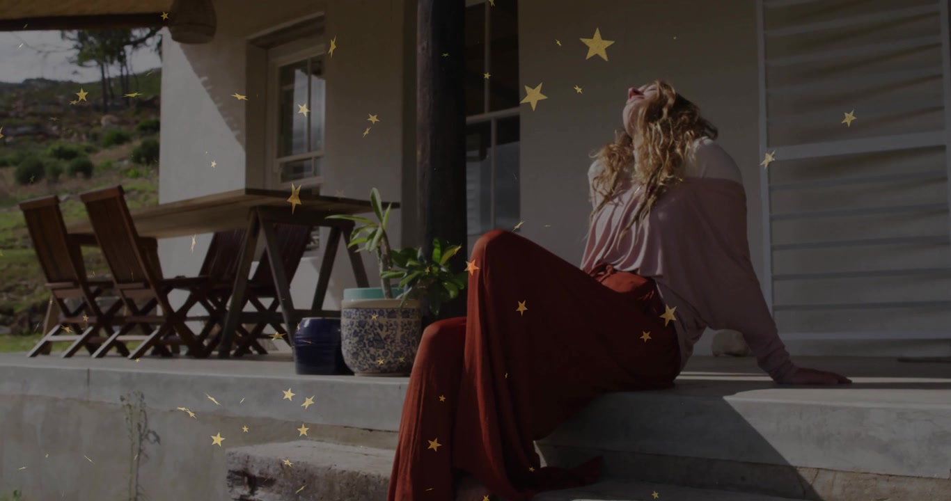 Donna che si appoggia all'indietro su un portico di cemento guardando il cielo mentre stelle dorate scendono, migliorando la salute