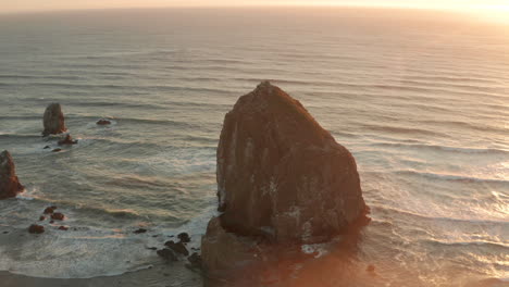 circling aerial shot of haystack rock sea stack at sunset