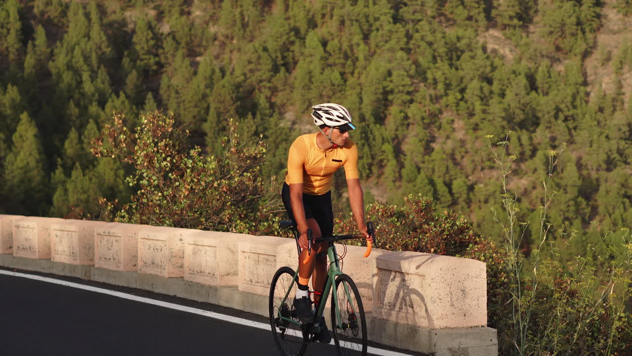 A guy wearing a yellow shirt is riding a sports road bike on a road that is situated at a high elevation in the mountains