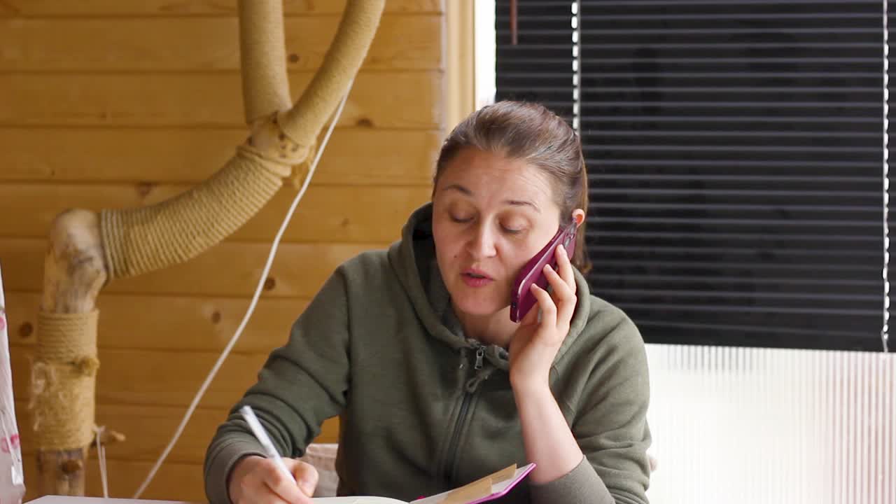 Young woman working from home talking on phone and taking notes, tilt down