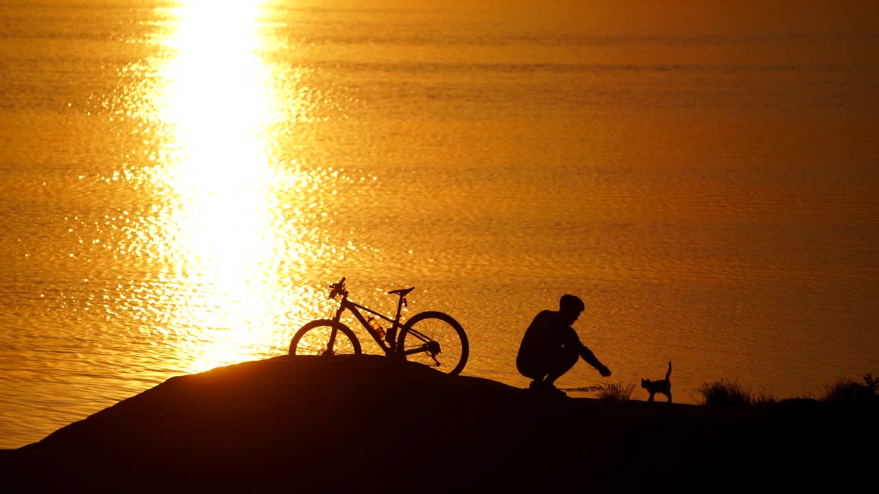 Man with bicycle resting on beach. Silhouette of man resting after cycling trip near river